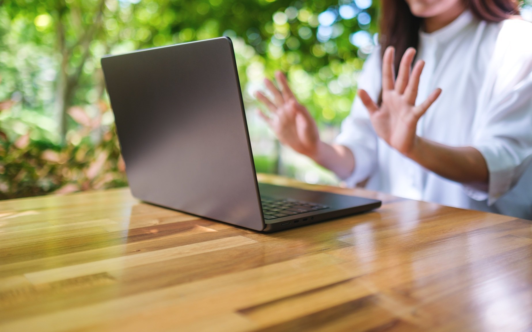 woman-gesturing-at-laptop-on-wood-table-outside-2026-03-25-09-11-56-utc