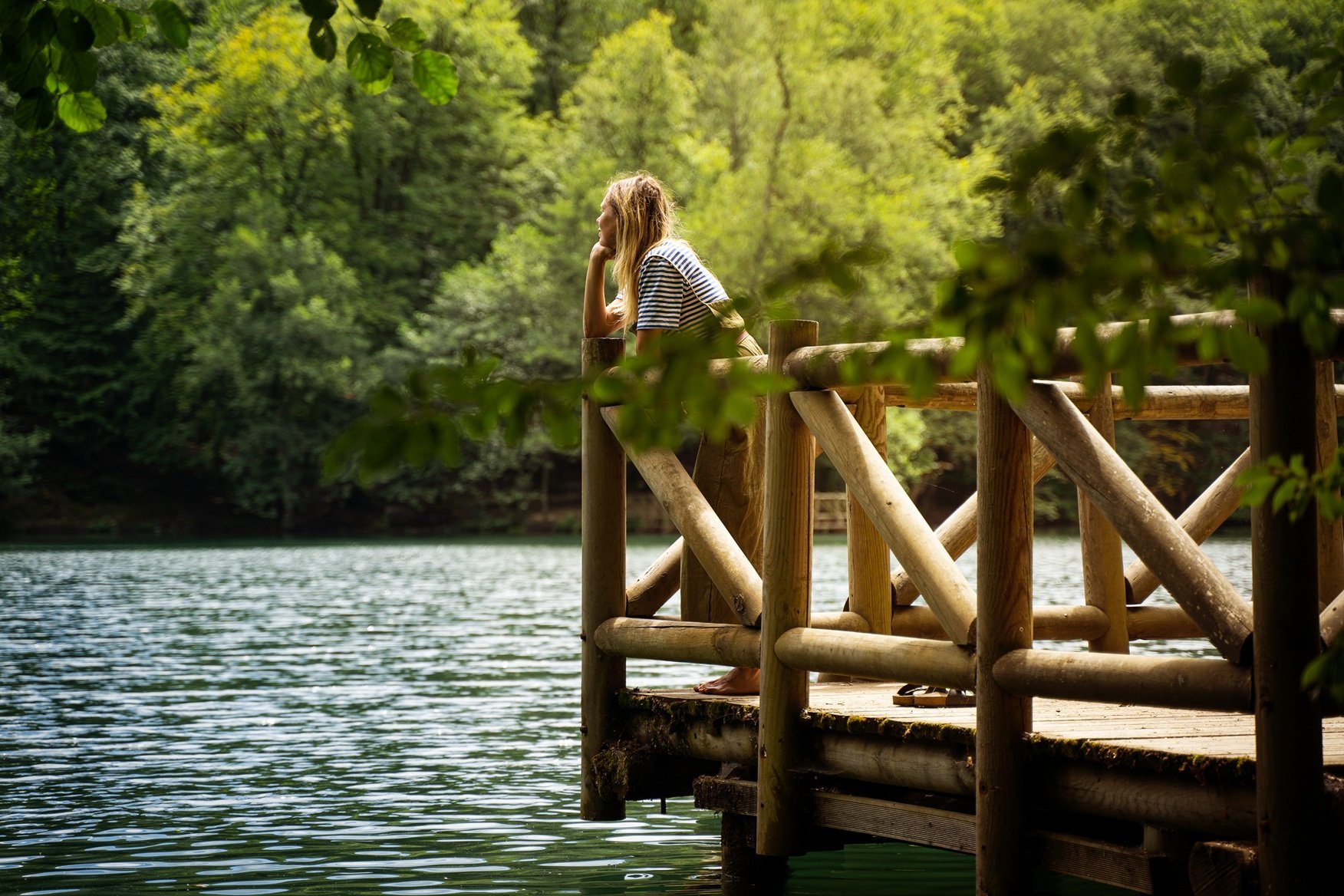 woman-relaxing-on-wooden-dock-by-lake-surrounded-b-2026-01-07-01-38-57-utc